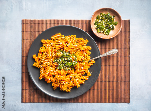 Curly pasta macaroni with tomato and gremolata sauce in a round dark plate on a table. Ready to eat. photo