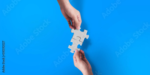 Two hand joining two matching puzzle pieces on blue background, conceptual image of teamwork.
