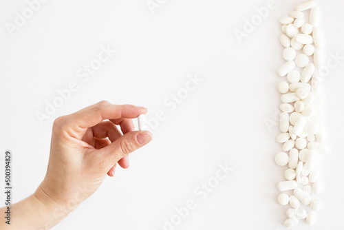 Biała tabletka trzymana w dłoni, białe lekarstwa i witaminy w tabletkach rozsypane na jasnym tle, suplementacja diety, leczenie przewlekłe, farmacja photo