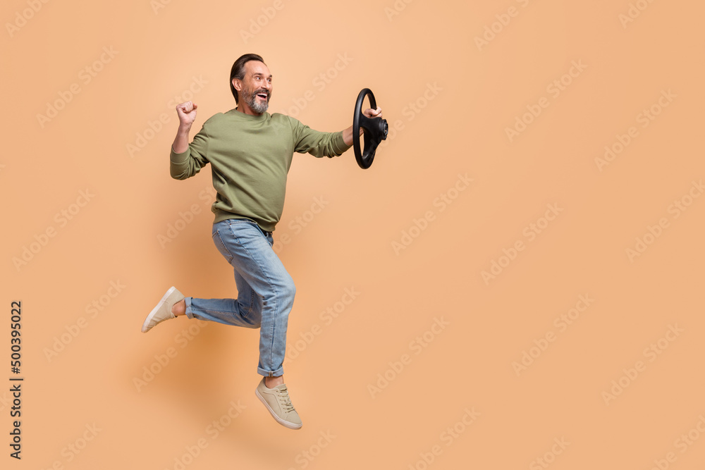 Full length profile photo of excited cheerful man look empty space vehicle wheel isolated on beige color background Full length profile photo of excited cheerful man look empty space vehicle wheel isolated on beige color background