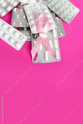 Różowa wstążeczka i blistry z lekarstwami i witaminami na różowym tle, leczenie nowotworów, rak piersi, amazonki