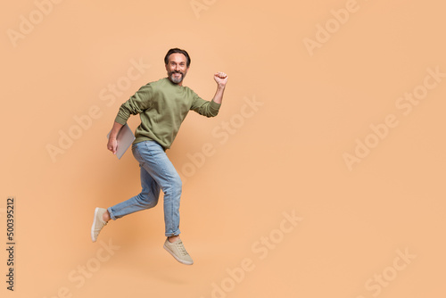 Full length portrait of handsome excited man hold netbook rush fast isolated on beige color background