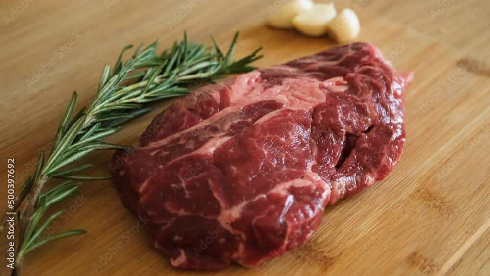 Juicy beef meat with garlic and rosemary ready to cook on wooden cutting board at kitchen. Uncooked raw prime steak with garlic. Close up delicious, modern cuisine Juicy beef meat with garlic and rosemary ready to cook on wooden cutting board at kitchen. Uncooked raw prime steak with garlic. Close up delicious, modern cuisine