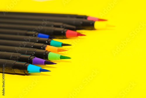 Multi-colored stationery felt-tip pens and brushes on a background of multi-colored cardboard paper.