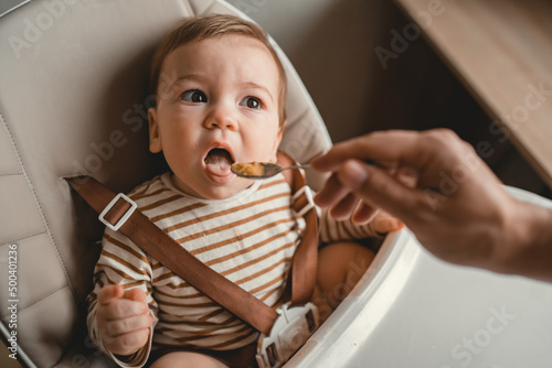 parent gives healthy food to his adorable child in the highchair in the kitchen empty space