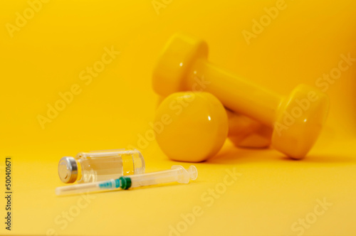 syringe and a jar of clear liquid with dumbbells on a yellow background, a horizontal picture. the concept of doping in sports, steroids, testosterone and other drugs banned in sports.