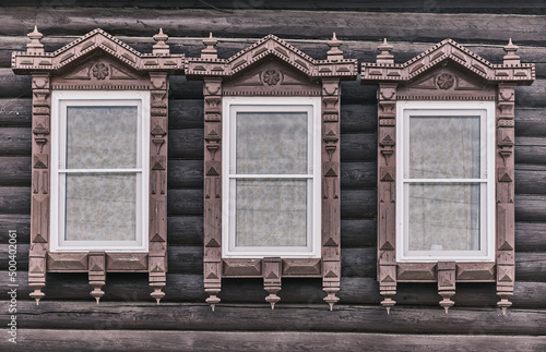 Wndows with carved wooden architraves. Log facade of typical rural Russian house.