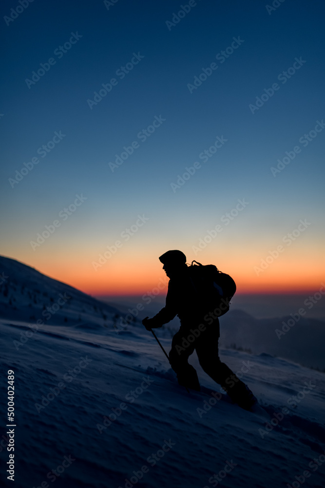 dark silhouette of male skier walking at snowy mountain against the background of the sky and sunset