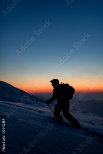 dark silhouette of male skier walking at snowy mountain against the background of the sky and sunset