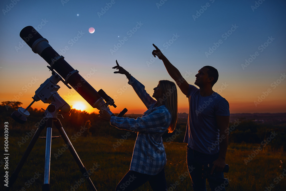 Couple stargazing together with a astronomical telescope.