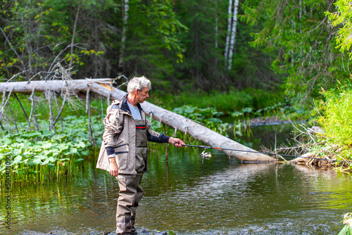 Portrait of fisherman in waders with spinning rod on the river. Spinning fishing photo