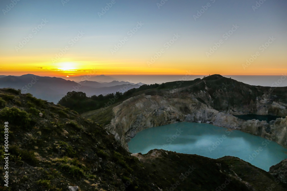 Sunrise over the Kelimutu volcanic crater lakes in Moni, Flores, Indonesia. Skyline is bursting with orange. Turquoise color of the lake. Golden hour colours the surroundings. Beauty of the nature - obrazy, fototapety, plakaty 
