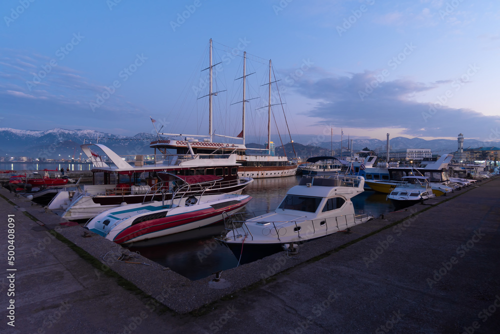 Boats, yachts in the harbor against the backdrop of snow-capped mountains at dusk, Batumi