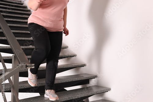 Overweight mature woman running downstairs indoors, closeup. Space for text photo