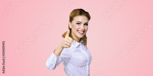 Portrait of happy smiling young excited businesswoman, showing thumb finger up or like hand sign gesture. Success in business concept studio shot. Rose pink color background. photo