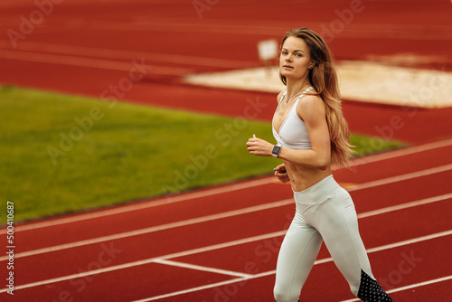 Athletic girl running at the stadium, working out, keep herself in shape, wearing sportswear, white top and pants, motivate doing sports, healthy lifestyle concept