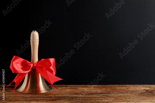 Golden bell with red bow on wooden table near blackboard, space for text. School days photo