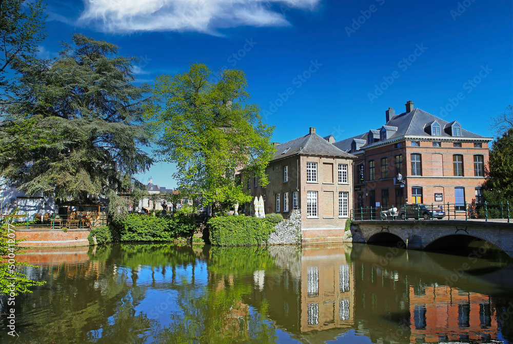 Lier, Belgium - April 9. 2022: View over water moat on park, medieval old houses, ancient stone bridge, blue sky