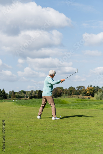 back view of senior asian man playing golf on field.