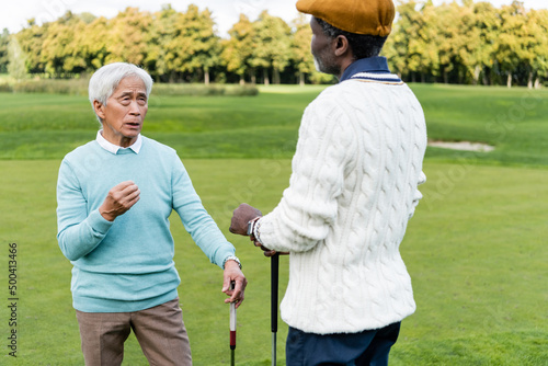 senior asian man talking with african american friend in flat cap.