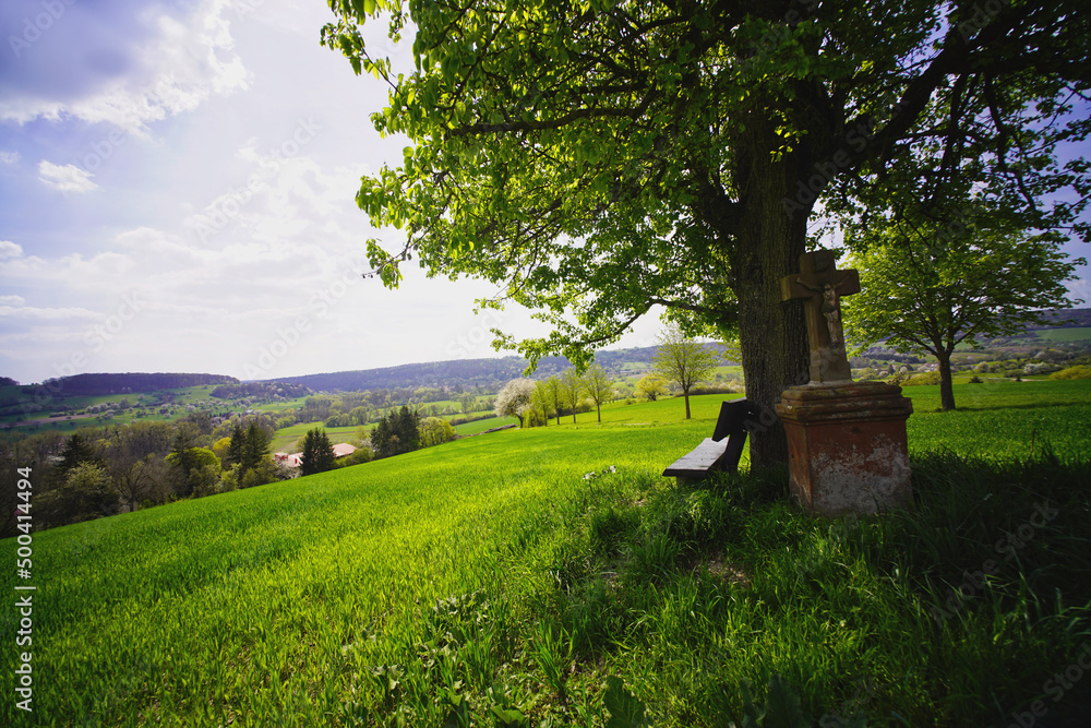 Aussichtsbank mit Wegkreuz über Gut Ritthof auf dem Alfred Döblin Weg im Bliesgau, Saarland Aussichtsbank mit Wegkreuz über Gut Ritthof auf dem Alfred Döblin Weg im Bliesgau, Saarland
