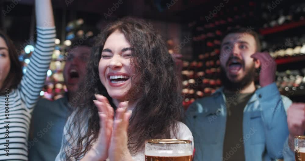 Group of young friends hang out in bar, watching TV and supporting sports team over glasses of beer. Tense moment results in cheers and applause, guys and girls hug, scream and laugh. Group of young friends hang out in bar, watching TV and supporting sports team over glasses of beer. Tense moment results in cheers and applause, guys and girls hug, scream and laugh.