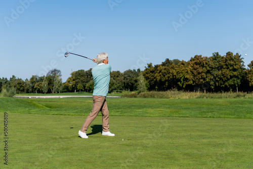 full length of asian senior man playing golf on green lawn.