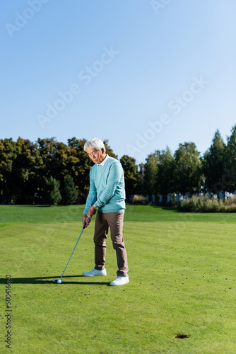 asian senior man holding golf club while playing outdoors.