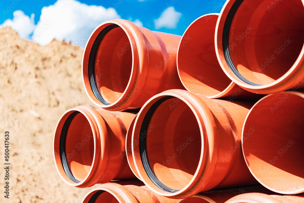 Orange sewer pipes at the construction site against the background of sand and blue sky. Preparation for the installation of an underground sewer system. Orange sewer pipes at the construction site against the background of sand and blue sky. Preparation for the installation of an underground sewer system.