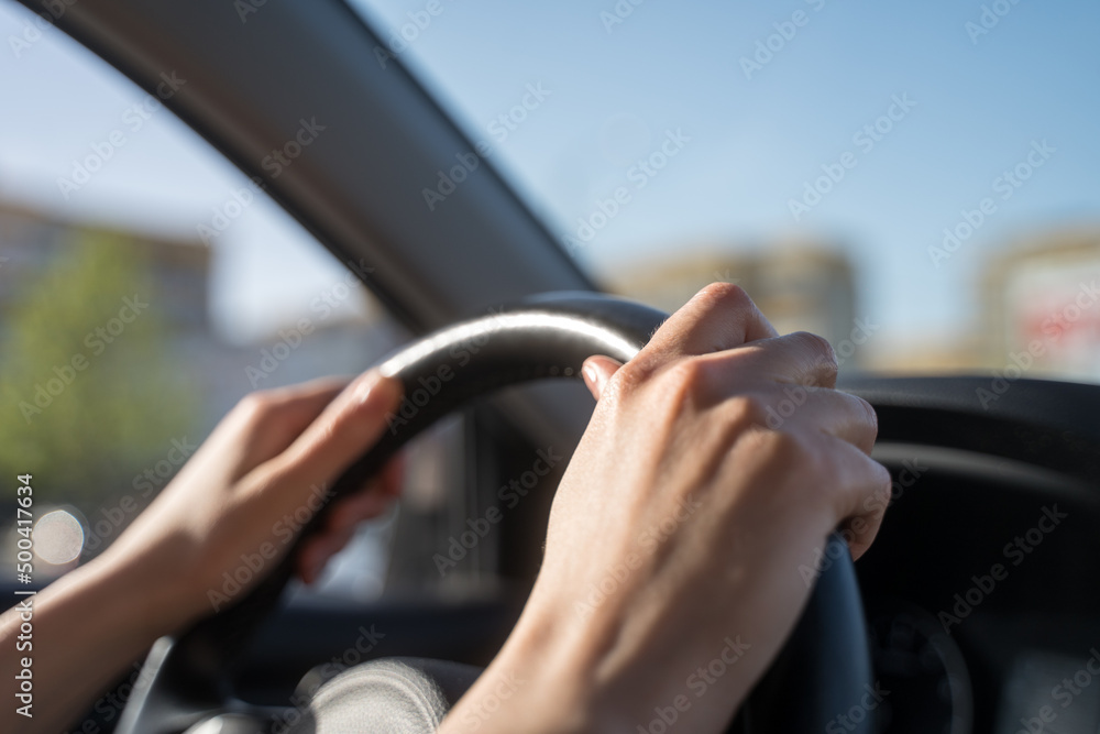 Hands of the female driver on the steering wheel of the car. Traffic control in motion, close-up