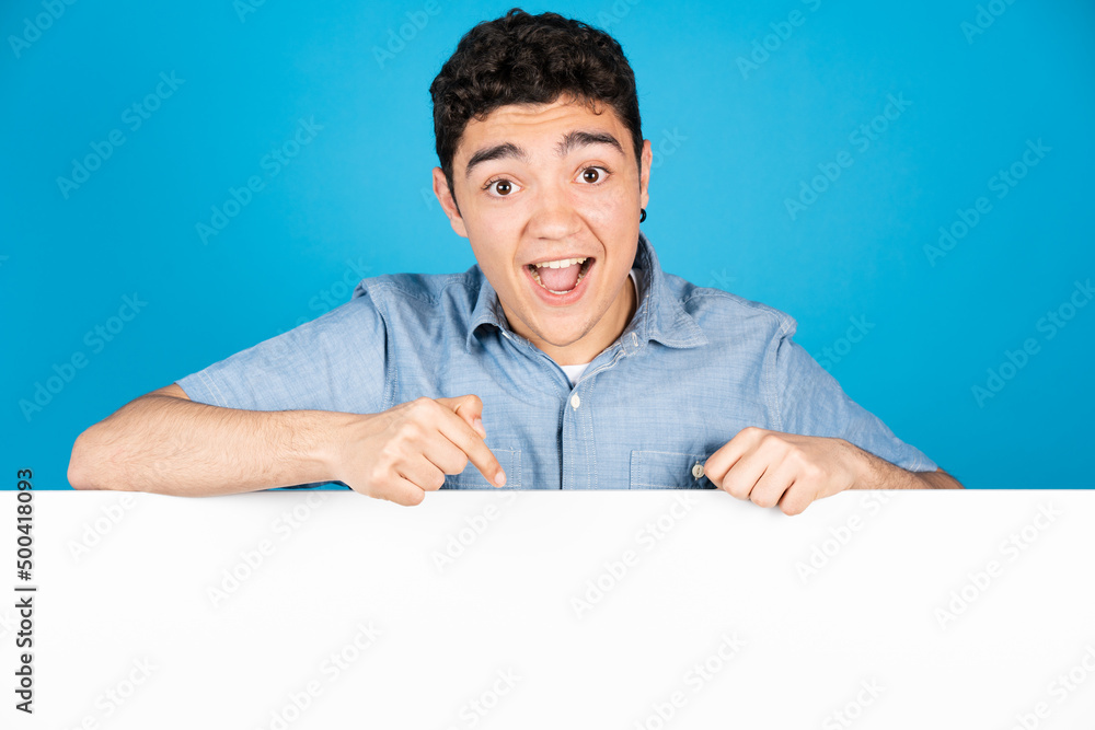 Happy hispanic young man pointing down to white copy space isolated on blue background Happy hispanic young man pointing down to white copy space isolated on blue background