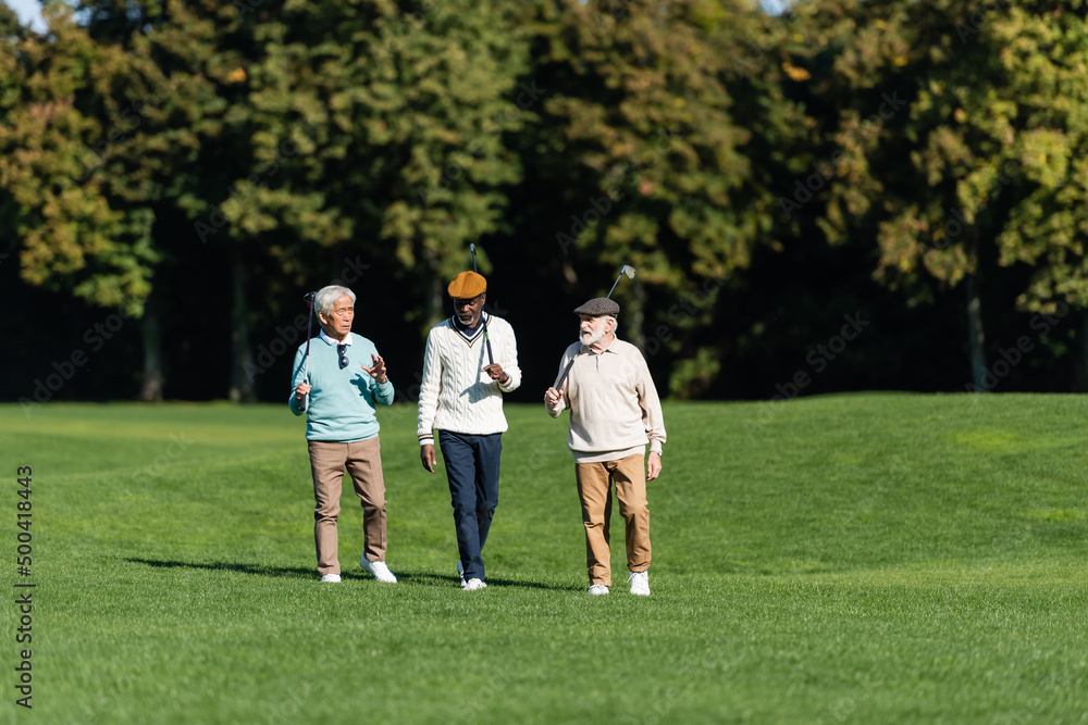 interracial senior friends walking with golf clubs on field. interracial senior friends walking with golf clubs on field.