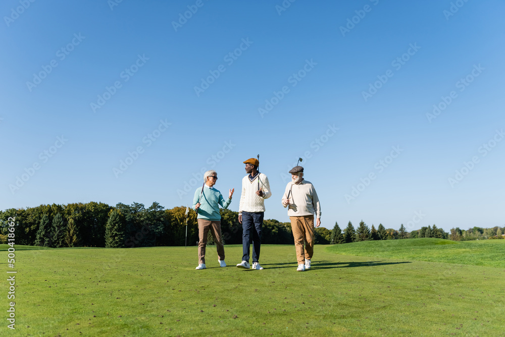 senior interracial friends walking with golf clubs on field. senior interracial friends walking with golf clubs on field.