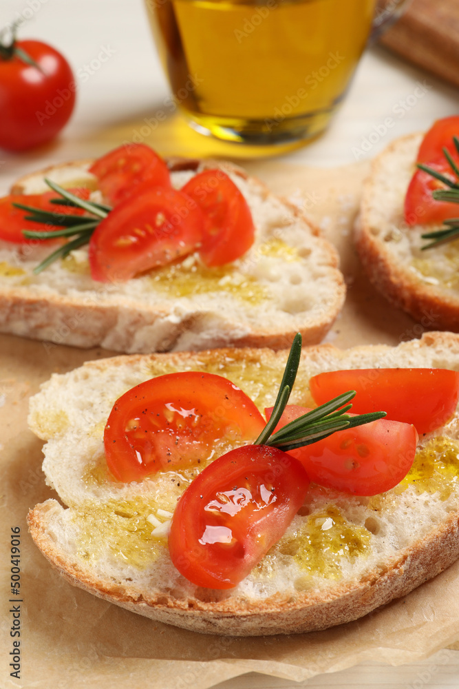 Tasty bruschettas with oil, tomatoes and rosemary on parchment paper, closeup Tasty bruschettas with oil, tomatoes and rosemary on parchment paper, closeup