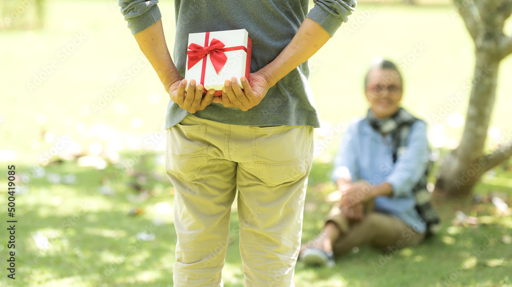 Naklejka premium Asian Lifestyle senior couple surprise gift for special day in the nature park happy and relax time. Elderly family the rest and chill after retirement in vacations.
