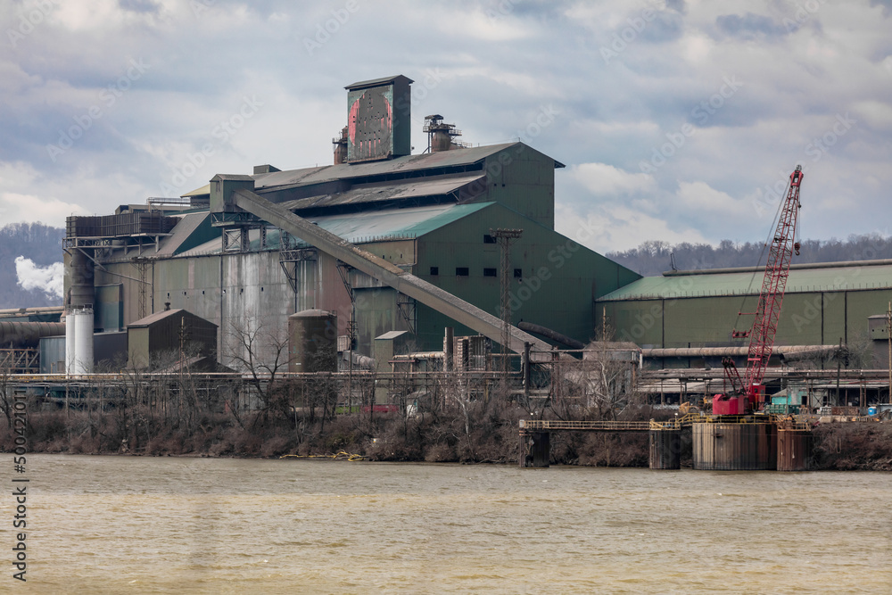 Large green factory building on edge of river Large green factory building on edge of river