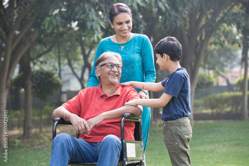 Mother and son with old man in wheelchair at park