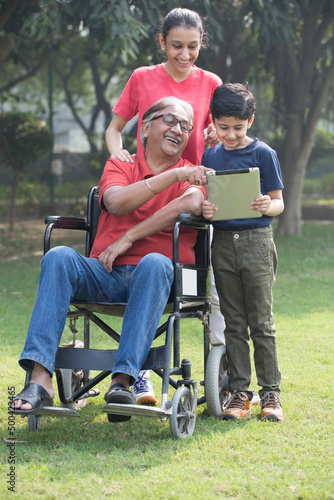 Happy grandfather in a wheelchair check a digital tablet with granddaughter at park © G-images