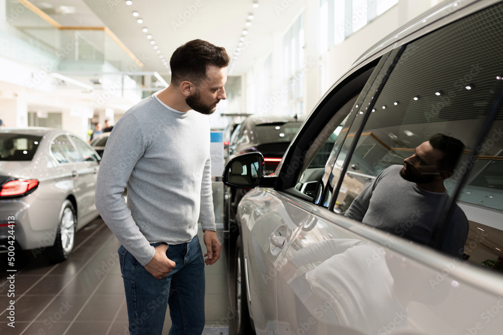 a man examines the range of cars in the showroom for a car dealership a man examines the range of cars in the showroom for a car dealership