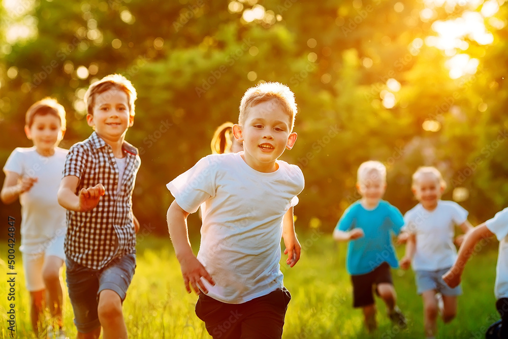 Fototapeta premium A group of happy children of boys and girls run in the Park on the grass on a Sunny summer day.
