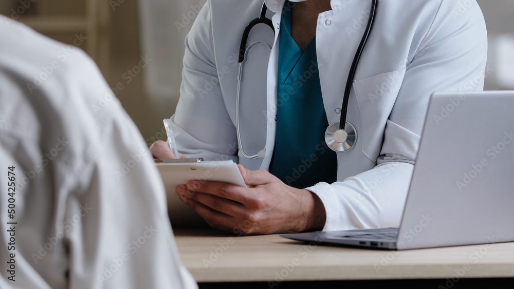 Close-up view male unknown doctor therapist man in white medical uniform sit at desk consult patient complaints give advice intern medical colleague explain treatment schedule handwriting prescription Close-up view male unknown doctor therapist man in white medical uniform sit at desk consult patient complaints give advice intern medical colleague explain treatment schedule handwriting prescription