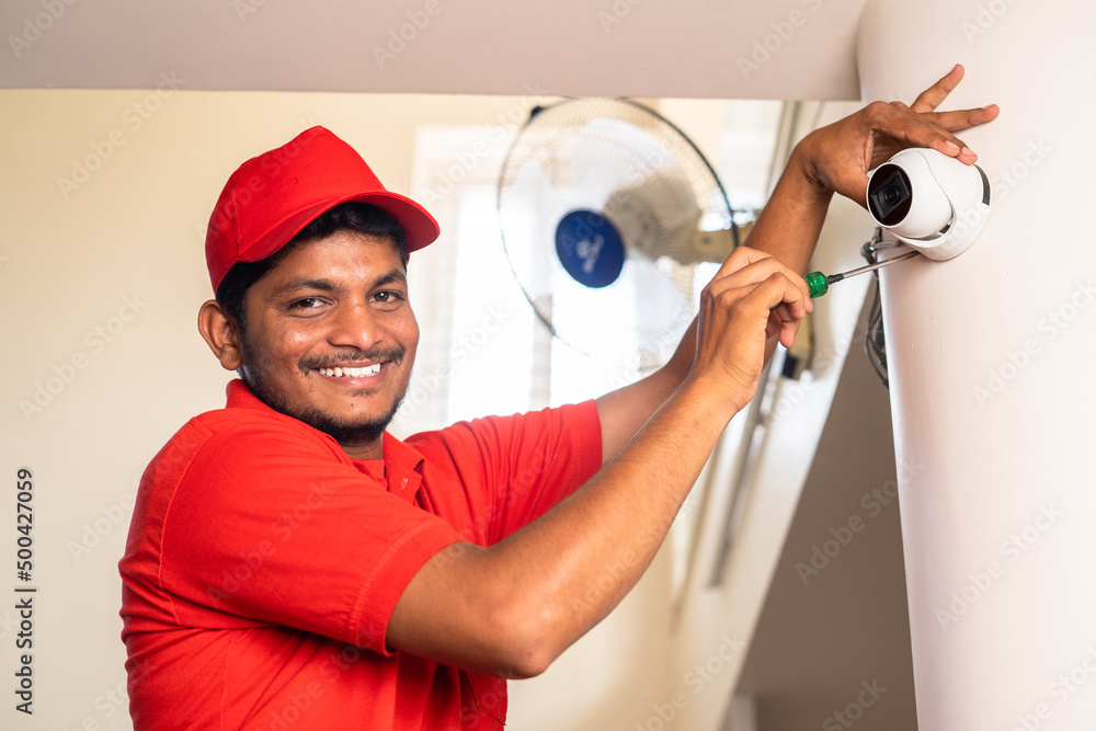 Happy smiling electrician looking at camera while fixing cctv surveillance camera at home - concept of professional occupation, expertise and employment. Happy smiling electrician looking at camera while fixing cctv surveillance camera at home - concept of professional occupation, expertise and employment.