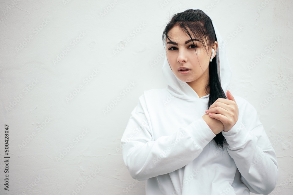 Woman dressed white hoodie kneads fists and wrists while training doing sport at the street in the morning. Sporty female athlete with wireless headphones Woman dressed white hoodie kneads fists and wrists while training doing sport at the street in the morning. Sporty female athlete with wireless headphones