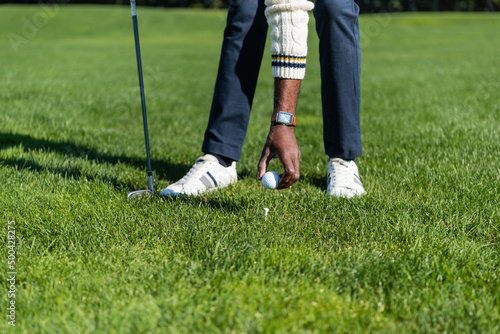 cropped view of african american man placing ball on golf tee.