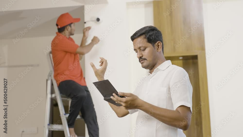 technician fixing angle or view of cctv camera while customer or owner checking in digital tablet at home - concept of employment, blue caller jobs and surveillance technology technician fixing angle or view of cctv camera while customer or owner checking in digital tablet at home - concept of employment, blue caller jobs and surveillance technology