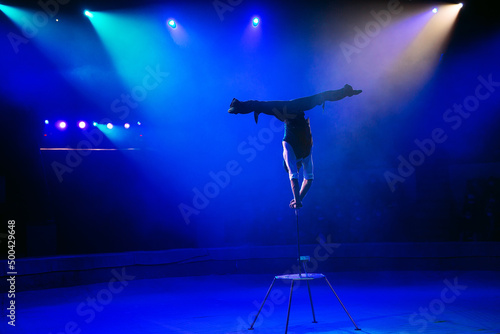A man of athletic build performs complex gymnastic exercises in the circus arena.