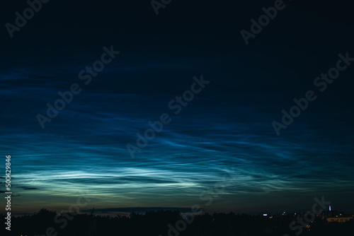 Noctilucent mesospheric clouds in night sky. Rare atmospheric phenomenon over city. photo