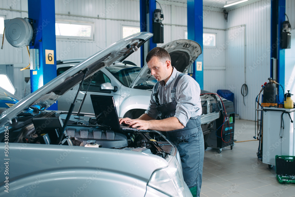 car mechanic using a computer laptop to diagnosing and checking up on car engines parts for fixing and repair. car mechanic using a computer laptop to diagnosing and checking up on car engines parts for fixing and repair.