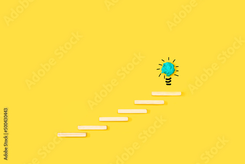 Escalera hechas de bloques de madera hacia una bombilla dibujada a mano sobre un fondo amarillo brillante y aislado. Vista de frente. Copy space. Concepto de idea, creatividad, ambición o éxito. photo