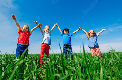 Happy Children on a green field with their hands up.